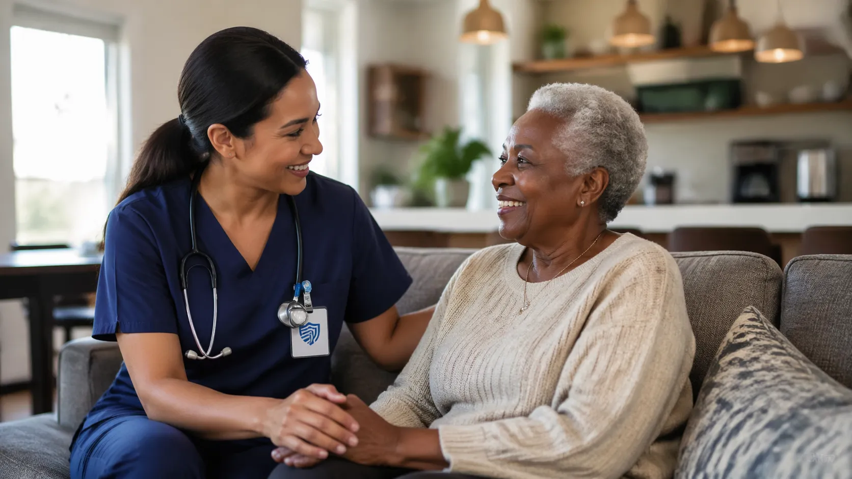 Healthcare professional holding hands with an elderly woman on a couch in a warm home setting